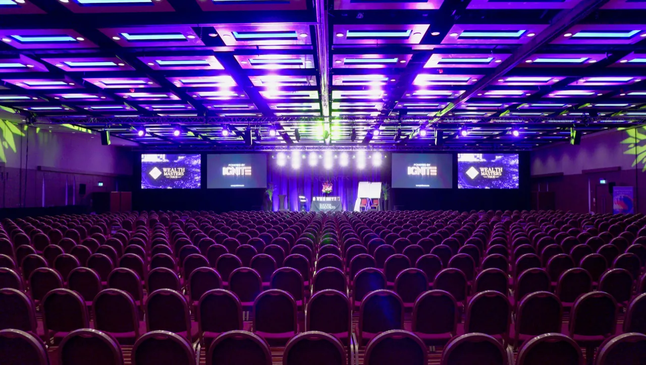 Hotel ballroom set theatre-style for hundreds, with 'Powered by IGNITE' and event screens either side of the stage
