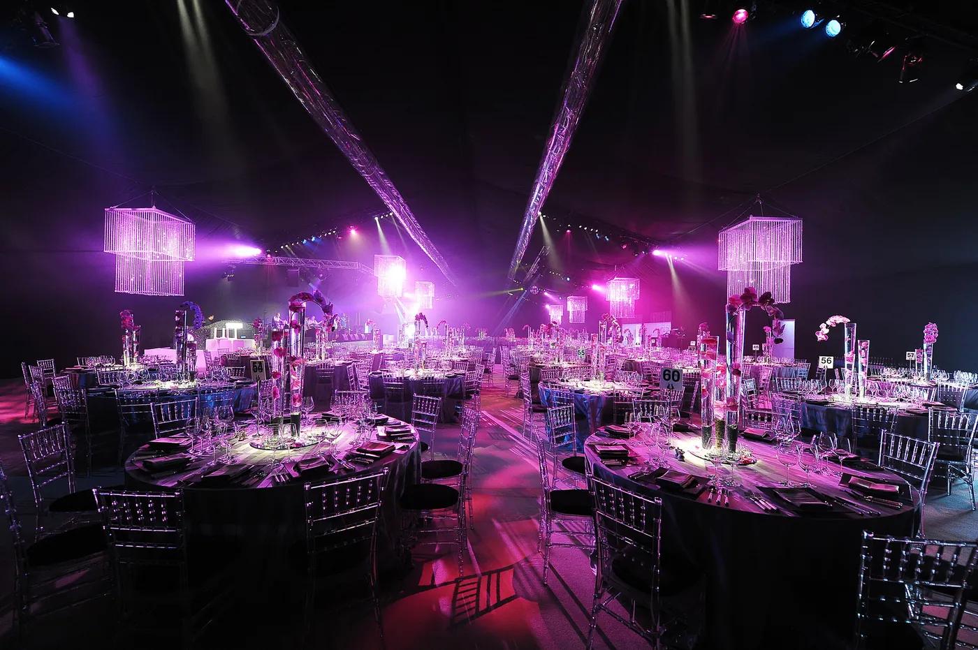 Private dinner in a marquee lit pink and purple, with crystal chandeliers, round tables and a stage