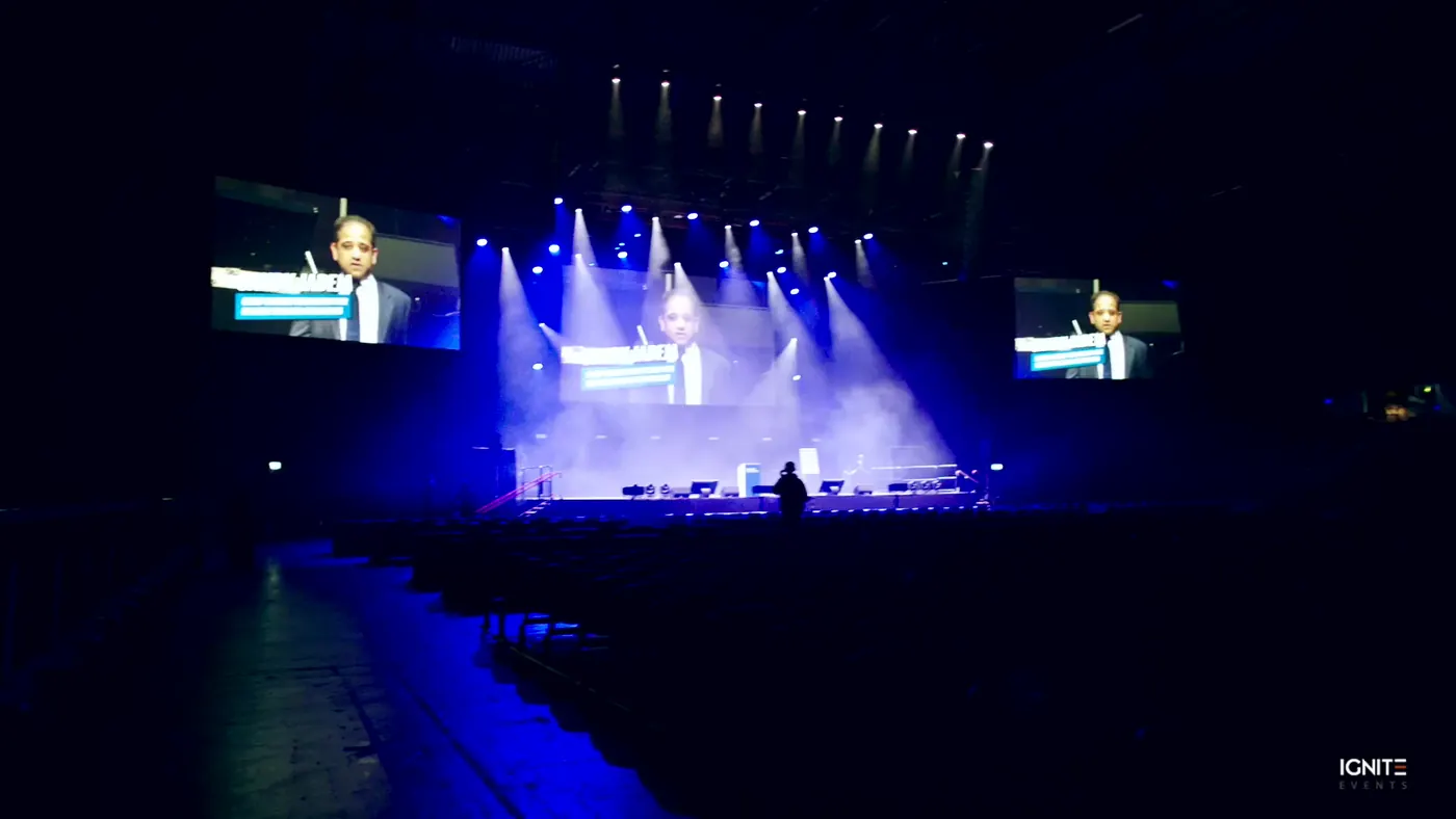 Speaker on stage between two side screens in a large hall