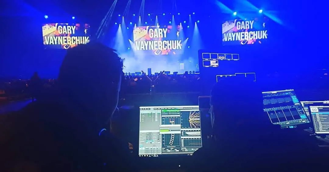 Control position at an arena show, with lighting and audio screens in front of a lit stage