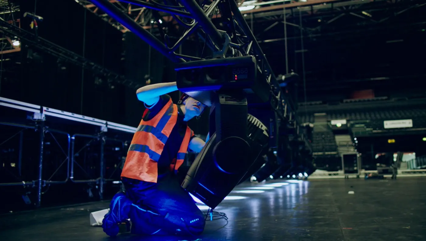 IGNITE technician kneeling to focus a moving light on a truss in an empty arena