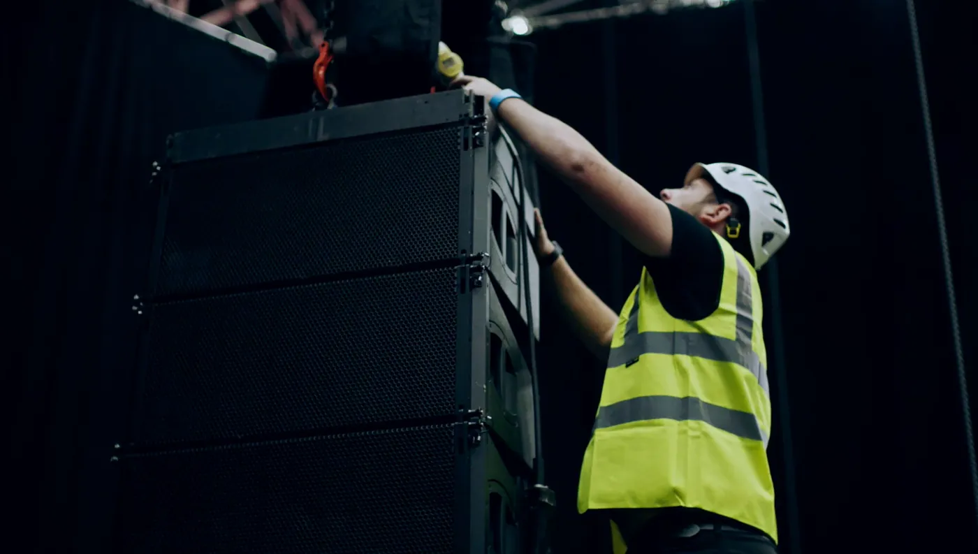 IGNITE technician in a hard hat rigging a flown line-array loudspeaker system