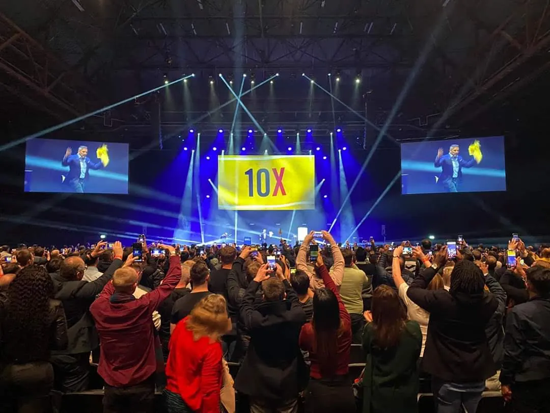 Arena audience on its feet filming on their phones as a speaker appears on the side screens