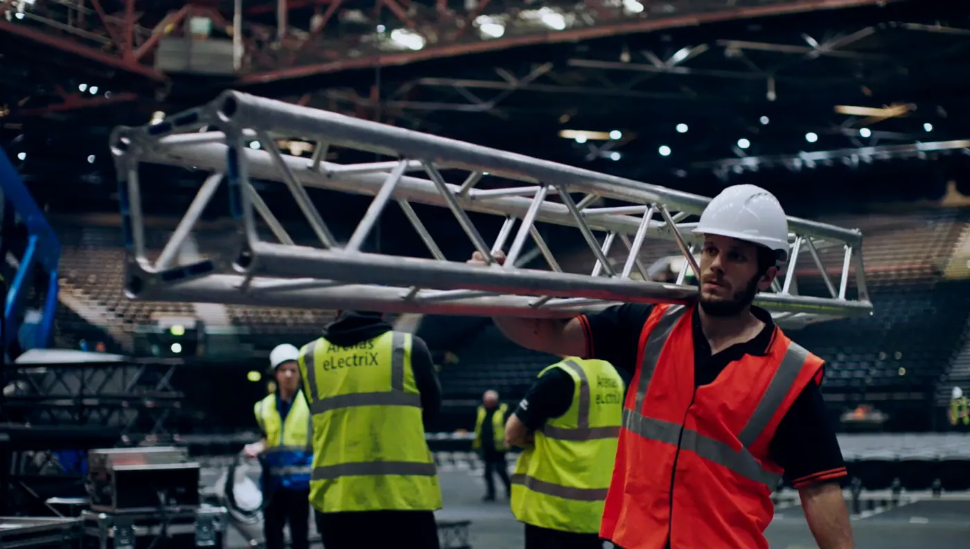 IGNITE crew member carrying aluminium truss across an arena floor during the build