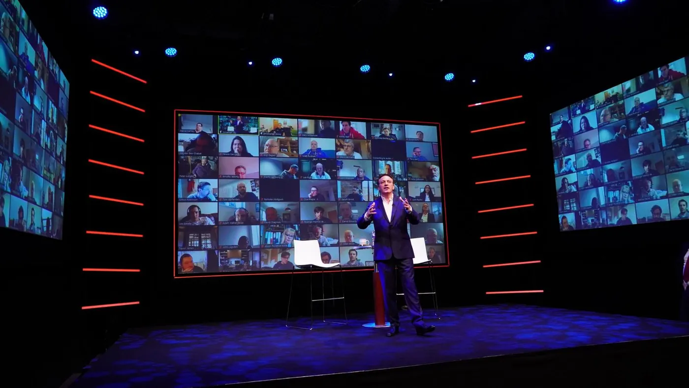 Presenter in front of an LED wall showing remote attendees, at IGNITE Studios